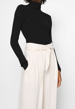 Zwarte geribde coltrui met lange mouwen, gecombineerd met lichtbeige hoge taille broek met een strikceintuur en twee zijzakken.