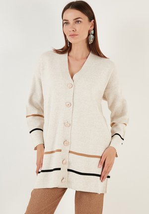 Beige cardigan with v-neck, button closure, and horizontal stripes in black and brown. Soft texture and relaxed fit.