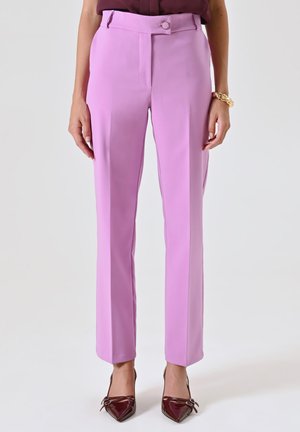Pantalons de costume lavande avec une coupe ajustée, texture lisse et une taille avec fermeture à bouton. Associés à des talons aiguilles bordeaux.