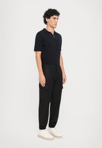 Marine polo skjorte med korte ærmer og lynlåsekrave, parret med tætsiddende sorte cargo bukser og hvide sneakers med en beige sål.
