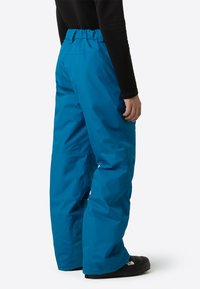 Modré voděodolné sněhové kalhoty s elastickým pasem, volným střihem a zesílenými manžetami u kotníků, doplněné černými zimními botami.