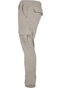 Hellbeige Cargo-Hosen aus Baumwolle. Mit schmal zulaufenden Beinen, Seitentaschen und elastischen Bündchen an den Knöcheln. Einfaches, utilitaristisches Design.