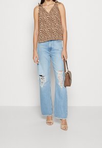 Top sans manches imprimé léopard marron, jeans droit déchirés bleu clair, sandales à talons beiges et sac à main marron.