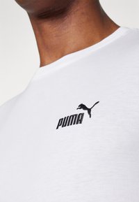 Witte katoenen T-shirt met een ronde hals, voorzien van een zwart geborduurd Puma-logo en tekst op de linkerkant van de borst. Gladde textuur.
