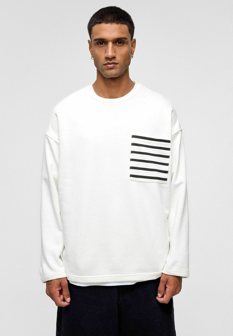 Witte sweatshirt met lange mouwen van zachte stof, heeft een voorkant linkerzak met zwarte horizontale strepen, losvallende pasvorm, ronde hals.