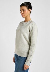 Sudadera gris claro con cuello redondo, puños y dobladillo acanalados, con un acabado texturizado. Combinada con una falda de mezclilla.