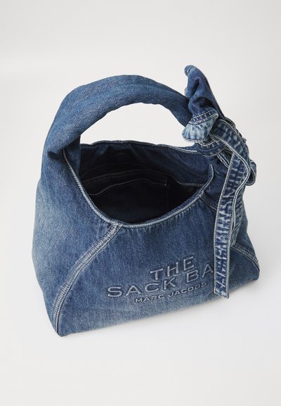 Borsa in denim con manico annodato, caratterizzata da una forma strutturata e testo ricamato. Il colore blu presenta una texture sbiadita.