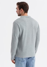 Grå långärmad polo skjorta i mjukt tyg. Har en standard krage och en avslappnad passform, kombinerad med ljusblå jeans.