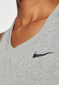Szara bezrękawnik sportowy z teksturowanym wykończeniem, z czarnym logo Nike na lewej stronie klatki piersiowej. Okrągły dekolt.