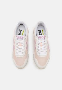 Sapatilhas rosa claro e brancas com materiais em malha e camurça, apresentando atacadores brancos, detalhes em rosa e uma sola texturizada com um logotipo.