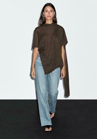 Brun, kortärmad stickad topp med en asymmetrisk design, i kombination med ljusblå, löst sittande jeans och svarta sandaler.
