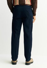 Sötétkék nadrág, sima textúrájú anyagból, egyenes szabással, oldalzsebekkel és klasszikus derékrésszel.