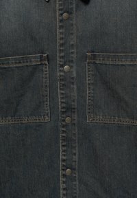 Donkerblauwe denim shirt met knoopsluiting aan de voorkant, twee grote borstzakken en contrasterende stiksels. Voorzien van metalen drukknoopjes en een zachte textuur.