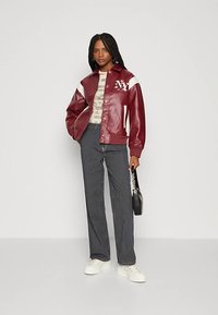 Bordowa skórzana kurtka varsity z białymi akcentami i logo "NY", zestawiona z paskowanymi spodniami i białymi trampkami, podkreślająca swobodny styl.