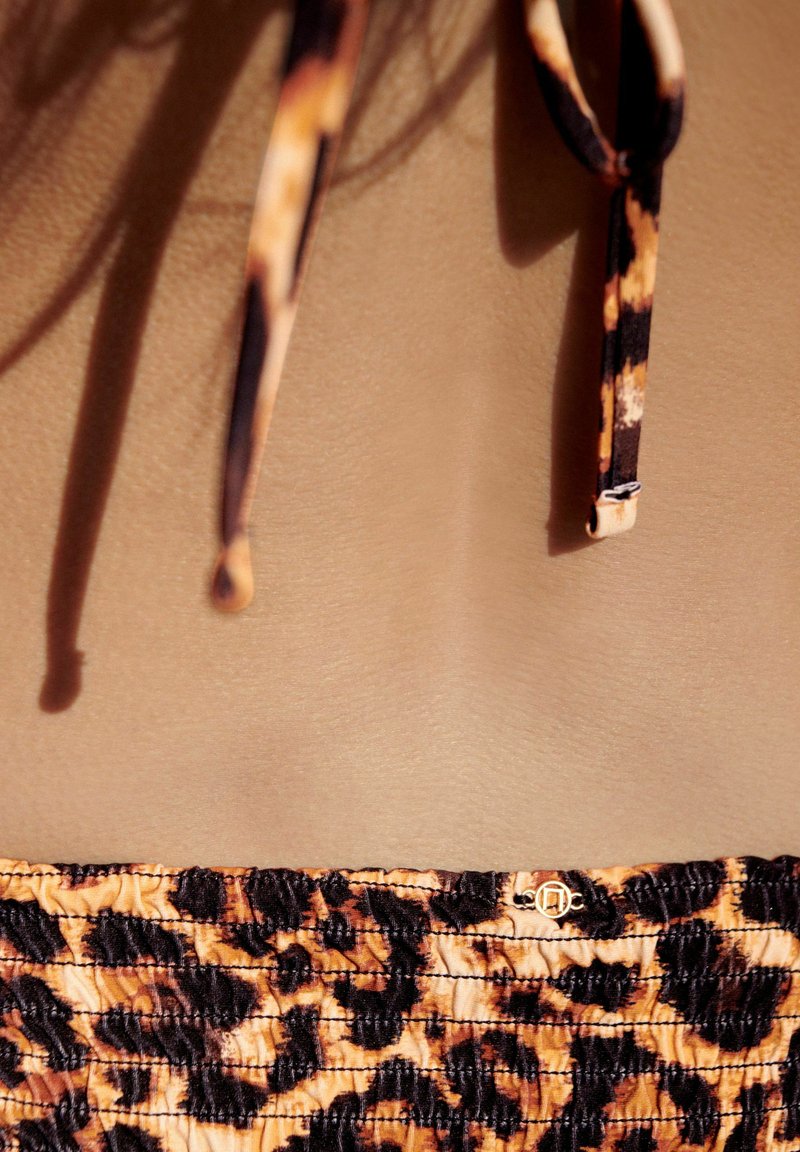 Top bikini con stampa leopardata in tonalità arancione, nera e marrone. Presenta spalline sottili e un accento decorativo dorato al centro. Tessuto texturizzato.