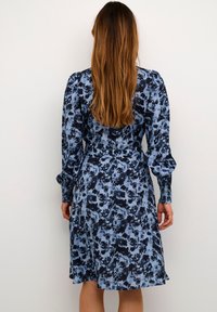 Rochie florală albastră cu mâneci lungi, talie ajustată și fustă vaporoasă. Prezintă un model abstract în nuanțe de albastru închis și albastru deschis.