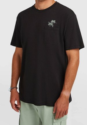 Man draagt een zwart T-shirt met korte mouwen met een klein palmboomontwerp boven de linkerborstzak en lichtgroene cargoshorts.
