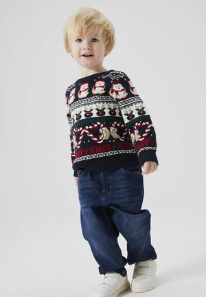 Maglione natalizio per bambini di colore blu navy con motivi festivi, tra cui pupazzi di neve e renne, abbinato a pantaloni di denim blu e sneakers bianche.