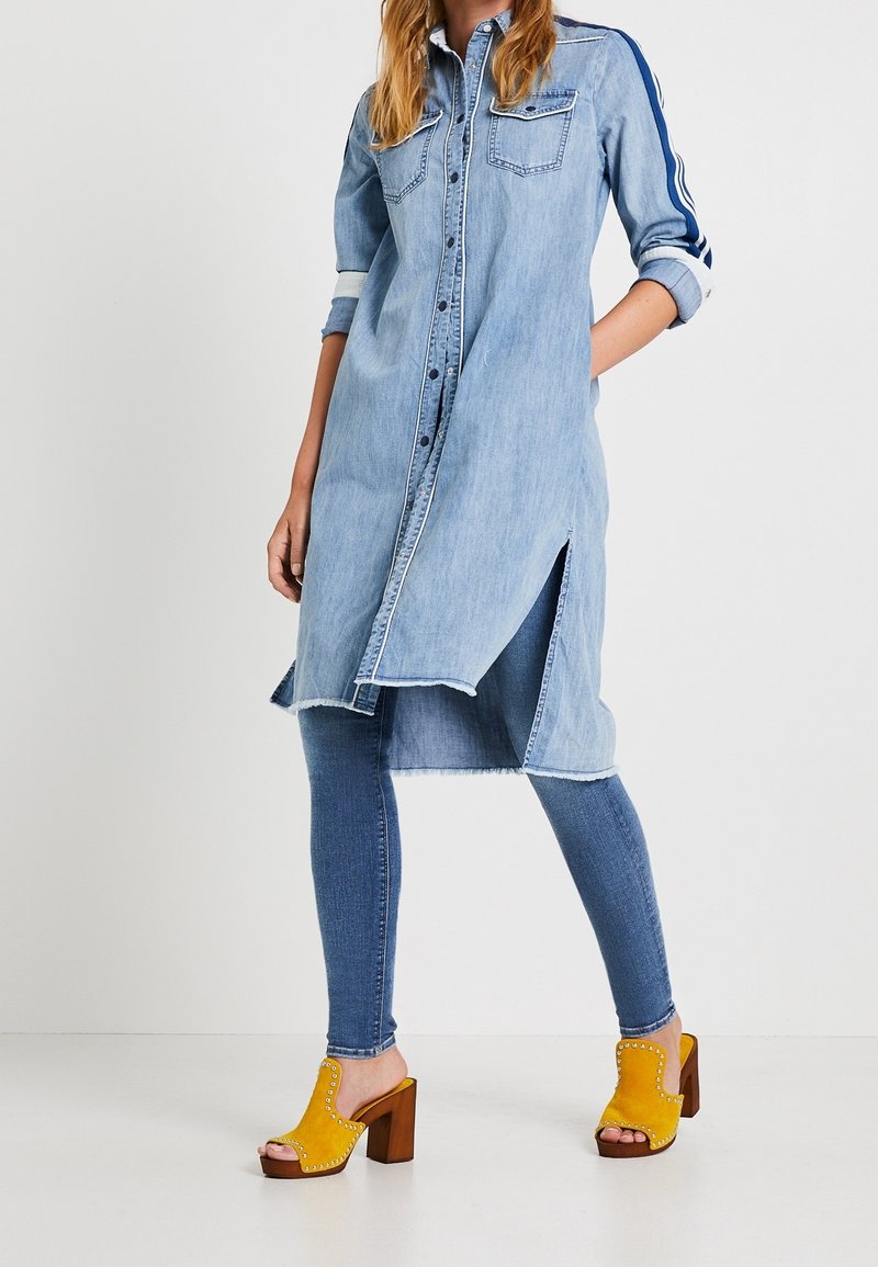 Ljusblå denimklänning med lång ärm, framknäppning, sidospår, i kombination med blå skinnyjeans och gula platåskor.