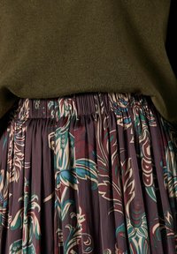 Vícebarevná plisovaná sukně s květinovým vzorem a elastickým pasem, zdobená fialovými, tyrkysovými a burgundskými vzory, doplněná tmavě zeleným svetrem.