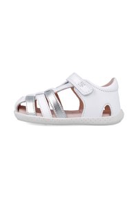 Sandalia blanca para niños hecha de cuero, con correas plateadas metálicas, cierre de velcro y suela de goma texturizada con orificios de ventilación.