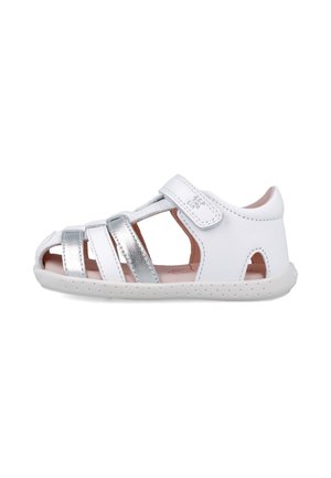 Sandalia blanca para niños hecha de cuero, con correas plateadas metálicas, cierre de velcro y suela de goma texturizada con orificios de ventilación.