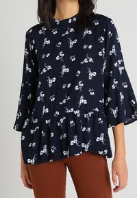 Blouse marine à imprimé floral, dotée d'un ourlet volanté et de manches cloche trois-quarts. Tissu doux avec une texture lisse.