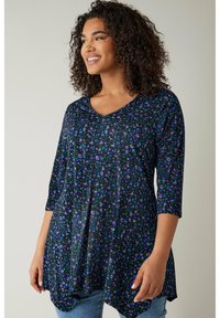 Schwarze Tunika mit V-Ausschnitt, die ein florales Muster in Lila und Grün aufweist. Sie hat Dreiviertelärmel und eine fließende Silhouette.