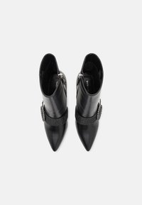 Botines negros de cuero con punta puntiaguda, banda de tela adornada y detalle de strass. Textura lisa, diseño elegante. Cierre de cremallera lateral.