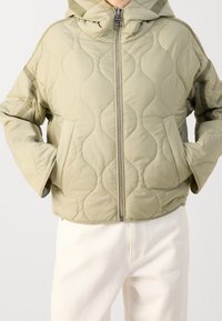 Veste matelassée vert clair avec capuche, dotée d'une fermeture éclair intégrale, de poches latérales et d'un motif ondulé texturé sur le tissu.