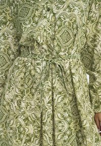 Groene geprinte jurk van luchtige stof met bloemen- en geometrische ontwerpen; heeft een gestrikte taille en een knoopsluiting aan de voorkant.