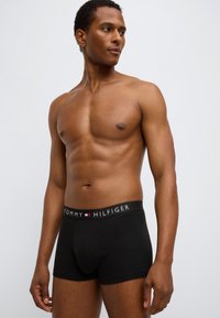 Μαύρα βαμβακερά μπόξερ με λογότυπο στη ζώνη μέσης που αναγράφει "TOMMY HILFIGER" με λευκό κείμενο, ραβδωτή υφή, εφαρμοστή γραμμή και κομμένη μέση στο ύψος του μηρού.