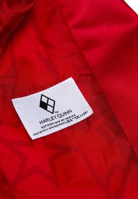 Červená saténová látka s bielou etiketou s čiernym textom a diamantom, ktorá uvádza "HARLEY QUINN" a súvisiace ochranné známky.