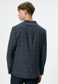 Mörkblå blazer i rutigt mönster, skräddarsydd passform, slagkragar och enkel ventspringa bak. Slät textur.