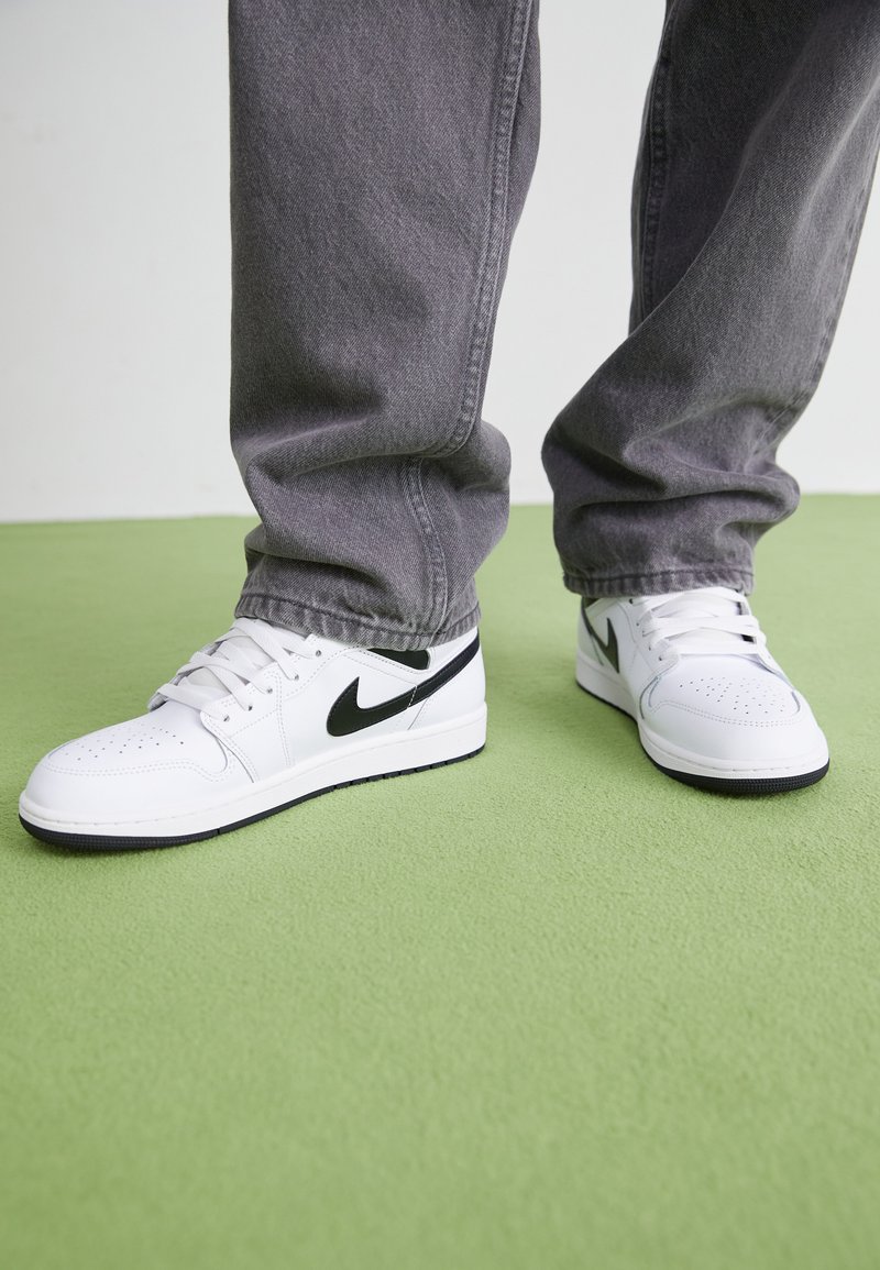 Sneakers bianchi in pelle con dettagli neri, punta perforata, lacci piatti, suola in gomma tonda e logo Nike visibile sui lati.