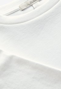 Primo piano dello scollo di una T-shirt bianca in cotone con una piccola etichetta bianca del marchio cucita all'interno del colletto.