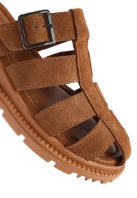 Sandal in suede marrone con più cinturini e una fibbia. La parte superiore testurizzata contrasta con la soletta liscia e la suola in gomma.