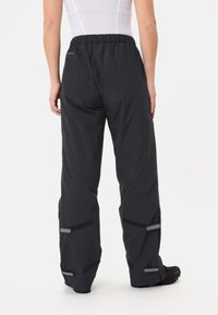 Pantalons imperméables noirs avec une coupe décontractée, dotés d'une taille élastiquée, d'accents réfléchissants et de sangles ajustables aux chevilles pour un maintien sécurisé.