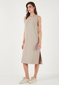 Beige midi šaty bez rukávů s kulatým výstřihem a bočními rozparky, vyrobené z měkké tkaniny, doplněné světlými teniskami.