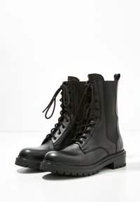 Černé kožené kotníkové boty na šněrování s kulatou špičkou, strukturovanými bočními panely, silnou gumovou podrážkou a kontrastním prošitím.