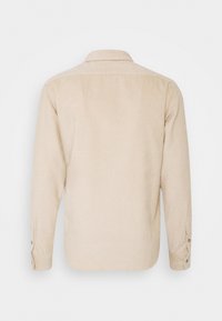 Beżowa sztruksowa koszula z prostym tyłem, długimi rękawami, zapinanymi na guziki mankietami i klasycznym kołnierzem. Materiał o fakturze z pionowymi prążkami.