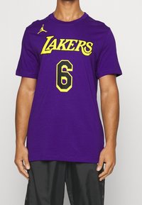 Muž v fialovém tričku Los Angeles Lakers s žlutým a černým číslem 6 a malým žlutým logem Jumpman na horním levém rohu.