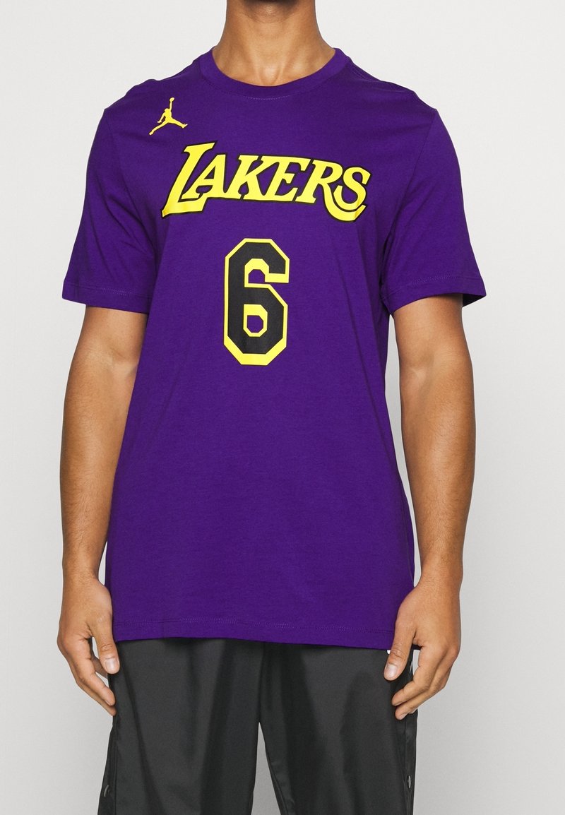 Muž v fialovém tričku Los Angeles Lakers s žlutým a černým číslem 6 a malým žlutým logem Jumpman na horním levém rohu.