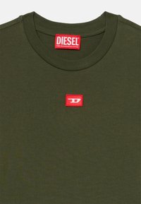 Olivinės spalvos medvilninė marškinėliai su apvaliu kaklu, trumpomis rankovėmis ir raudona "DIESEL" logotipo etikete kairiajame krūtinės šone. Lygi tekstūra visame paviršiuje.