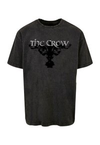 Must have mustar T-särk, millel on hall "The Crow" graafika, tekstuuri viimistlusega ja lühikeste varrukatega. Lõdvestatud istuvus ja ümar kaelus.