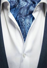 Blå paisley-mönstrad scarf instoppad i en vit skjorta, med en mörk kavaj synlig i kanterna, som visar upp ett slätt tyg och en strukturerad design.