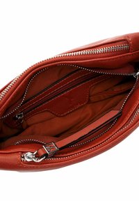 Sarkanas ādas rokassomas iekšpuse ar gludu tekstūru, ietver vairākas nodalījumus un kabatas ar rāvējslēdzējiem. Sudraba toņa metāla aksesuāri.