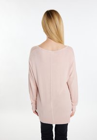 Maglione oversized rosa chiaro con una texture a coste, ampio scollo a barca, spalle abbassate e maniche lunghe, indossato sopra pantaloni neri.