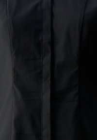 Čierny priliehavý odev s hladkou textúrou, s rovnou švami v strede, minimalistickým dizajnom a bez viditeľného hardvéru.