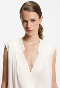 Weiße Seidenbluse mit tiefem V-Ausschnitt, kurzen Ärmeln, subtilen Falten und glatter Textur. Klare Linien und minimalistisches Design.